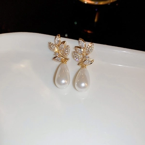 Macro shot of gold leaf earrings with sparkling zircons and white drop pearls