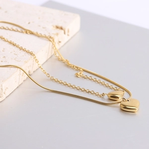 Dettaglio di una collana doppia dorata con pendenti a cuore su una lastra di pietra bianca