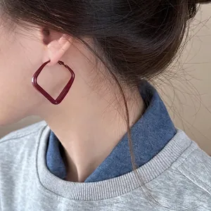 Close-up of deep red geometric square earrings with a glossy enamel finish on a model