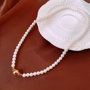 Close-up of white pearl necklace with gold spherical clasp on vintage ceramic plate