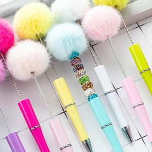 Creative beaded ballpoint pens with colorful plush pom-poms and crystal accents on a grid