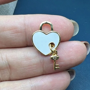 Macro shot of heart lock pendant with white enamel and a tiny gold key with zircon charm