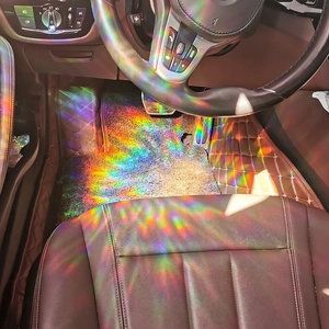 Rainbow light patterns from a suncatcher prism projected on brown leather car mats