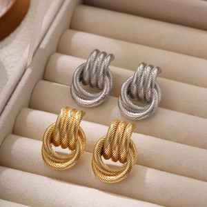 Macro shot of 18K gold and silver triple twisted wire knot stud earrings on a beige tray