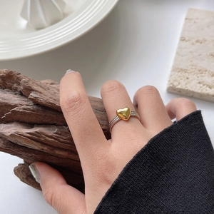 Minimalist gold heart ring on silver band worn by a model against a natural wood texture