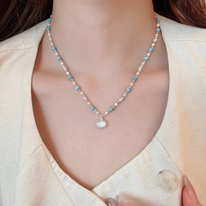 Dettaglio collana di perline blu e bianche con ciondolo circolare in madreperla chic