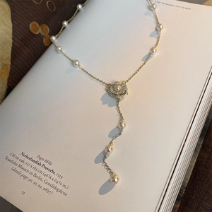 Détail du collier en Y doré avec perles, pendentif floral et pierres de zircon