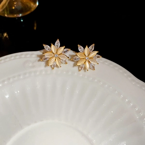 Macro shot of gold floral earrings with cat eye stones and zircons on a white plate
