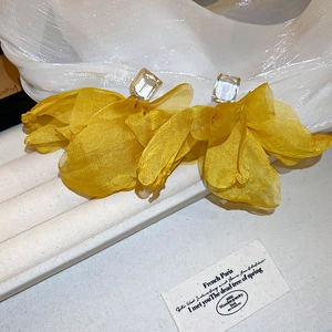 Detail of yellow fabric floral earrings with crystal studs on a white velvet display