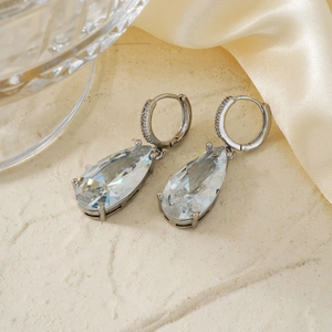 Macro detail of silver drop earrings with clear zircon stones on beige texture