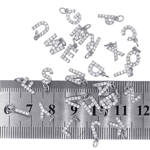 Detail showing 10mm silver letter charms with clear zircons next to a ruler for scale