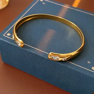 Gold stainless steel open bangle with rectangular and round cubic zirconia on a blue box