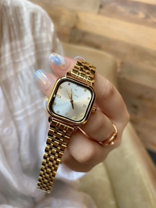 Detailed close-up of a square gold watch with a shimmering diamond-set dial and metal band