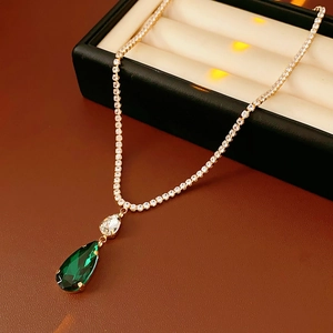 Macro shot of gold tennis necklace featuring green pear-cut zircon pendant on leather