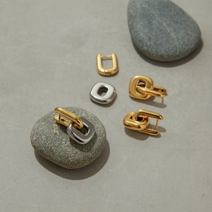 Polished gold and silver geometric U-shaped steel earrings on a grey stone surface