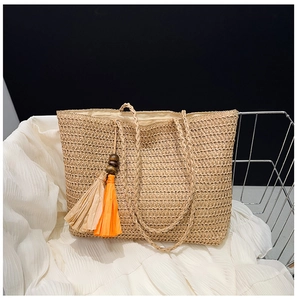 Detail of straw tote bag featuring beige weave texture with wooden bead and orange tassel