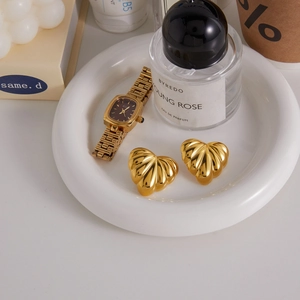 Detailed view of 18k gold heart earrings and vintage watch on a white ceramic plate