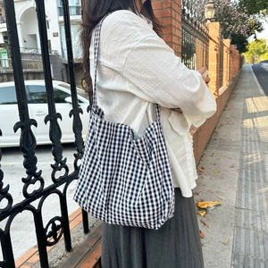 Close-up of black and white gingham canvas tote bag worn on shoulder in street style setting
