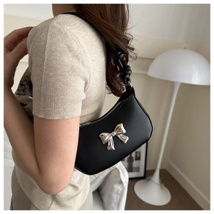 Close-up of a black leather underarm bag with a decorative silver metal bow on model