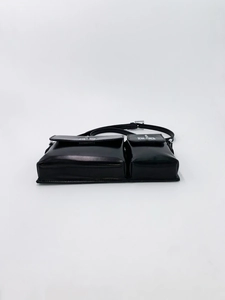 Detail of minimalist black leather baguette bag featuring double front pockets and silver buckles