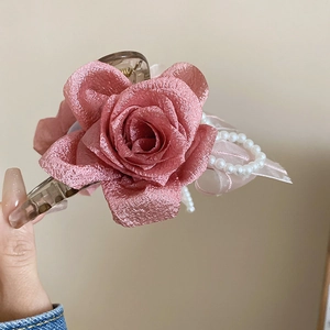 Dettaglio della molletta per capelli con rosa in tessuto rosa, perle e base trasparente