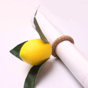 Macro view of artificial yellow lemon napkin ring with green leaves on white napkin