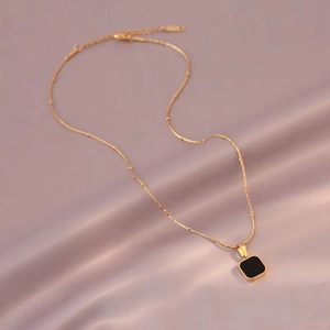 Minimalist gold necklace with square black pendant on satin fabric background