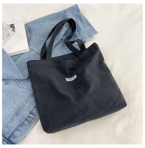 Detail of black canvas tote bag with FASHION label, styled with denim jacket and books