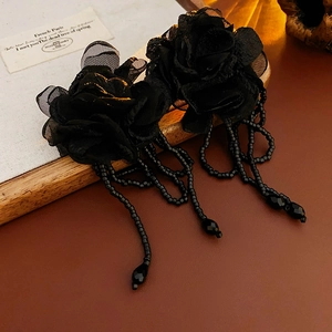 Detail of elegant black fabric flower earrings with long bead tassels on vintage wood frame