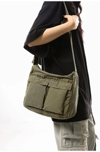 Detail of army green canvas messenger bag featuring vintage workwear style and dual front pockets