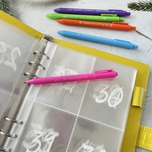 Detail of yellow budget binder with colorful pens featuring inspirational quotes