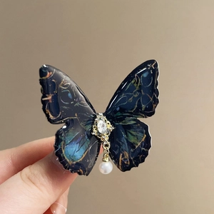 Detailed macro view of a butterfly hair clip with resin wings and a hanging pearl drop