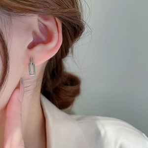 Close-up of geometric silver interlocking rectangular earrings on female model's ear