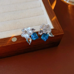 Close-up of floral stud earrings with blue square crystal and light blue waterdrop gem