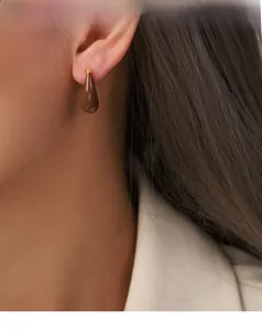 Detail view of a model wearing a dark brown enamel teardrop earring with gold finish