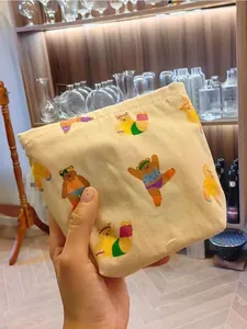 Detail of hand holding a beige canvas makeup bag with colorful cartoon bear prints
