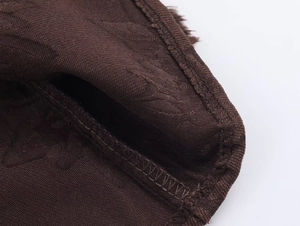 Detail der kaffeebraunen Jacquard-Stoffstruktur mit feinen Nähten am langen Kleid