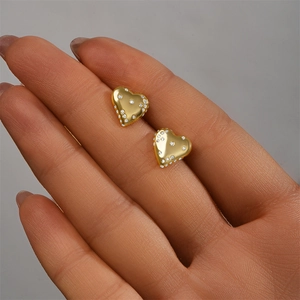 Close-up of heart-shaped gold stud earrings with cubic zirconia held by hand
