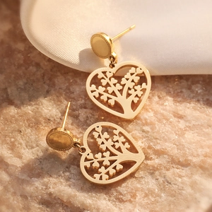 Golden tree of life heart drop earrings in titanium steel displayed on beige stone