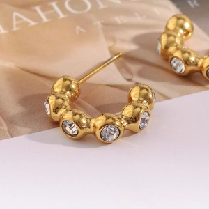 Macro shot of gold plated C-shaped earrings with inlaid zircons and clear crystals