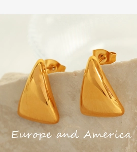 Close-up of golden triangular stud earrings with backings on a textured stone base