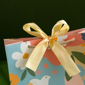 Floral paper gift bag with yellow ribbon bow and gold rope handles for festive presents