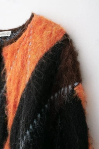 Gros plan sur la maille et le col d'un pull à motifs de losanges orange et noir