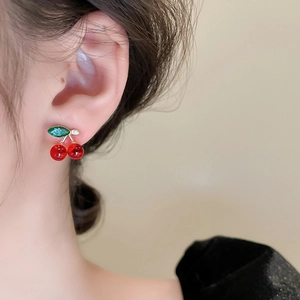 Close-up of red cherry stud earrings with green leaf detail worn by a female model