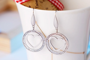 Detail shot of heart-shaped hollow earrings with inlaid zircons hanging on a cup