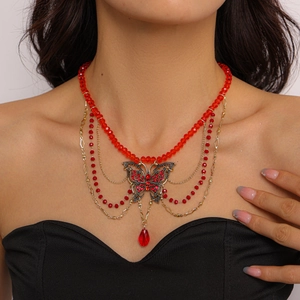 Detail of multi-layer necklace featuring red beads and gold butterfly pendant with crystals