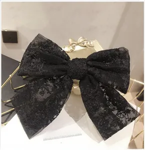 Detail of a large black lace bow hair clip with intricate floral mesh embroidery pattern