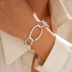 Close-up of textured oval links on a metallic chain bracelet worn over a beige shirt cuff