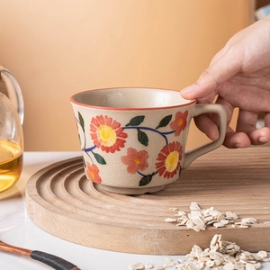 Floral ceramic mug with crackle glaze finish held by hand on a wooden tray
