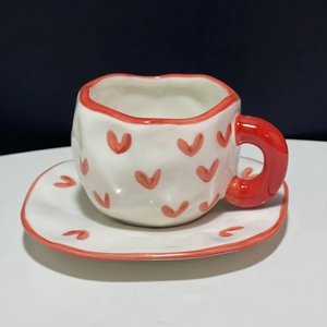 Detail shot of a handmade irregular ceramic coffee cup with red heart pattern and trim